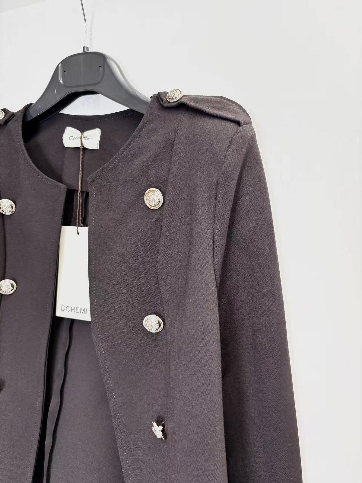 A dark brown double-breasted jacket with silver buttons, hanging on a black hanger with a white brand tag against a plain white background.