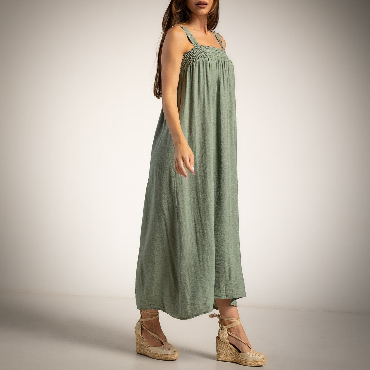 A woman modeling a green linen maxi dress with studded shoulder straps and a smocked bodice