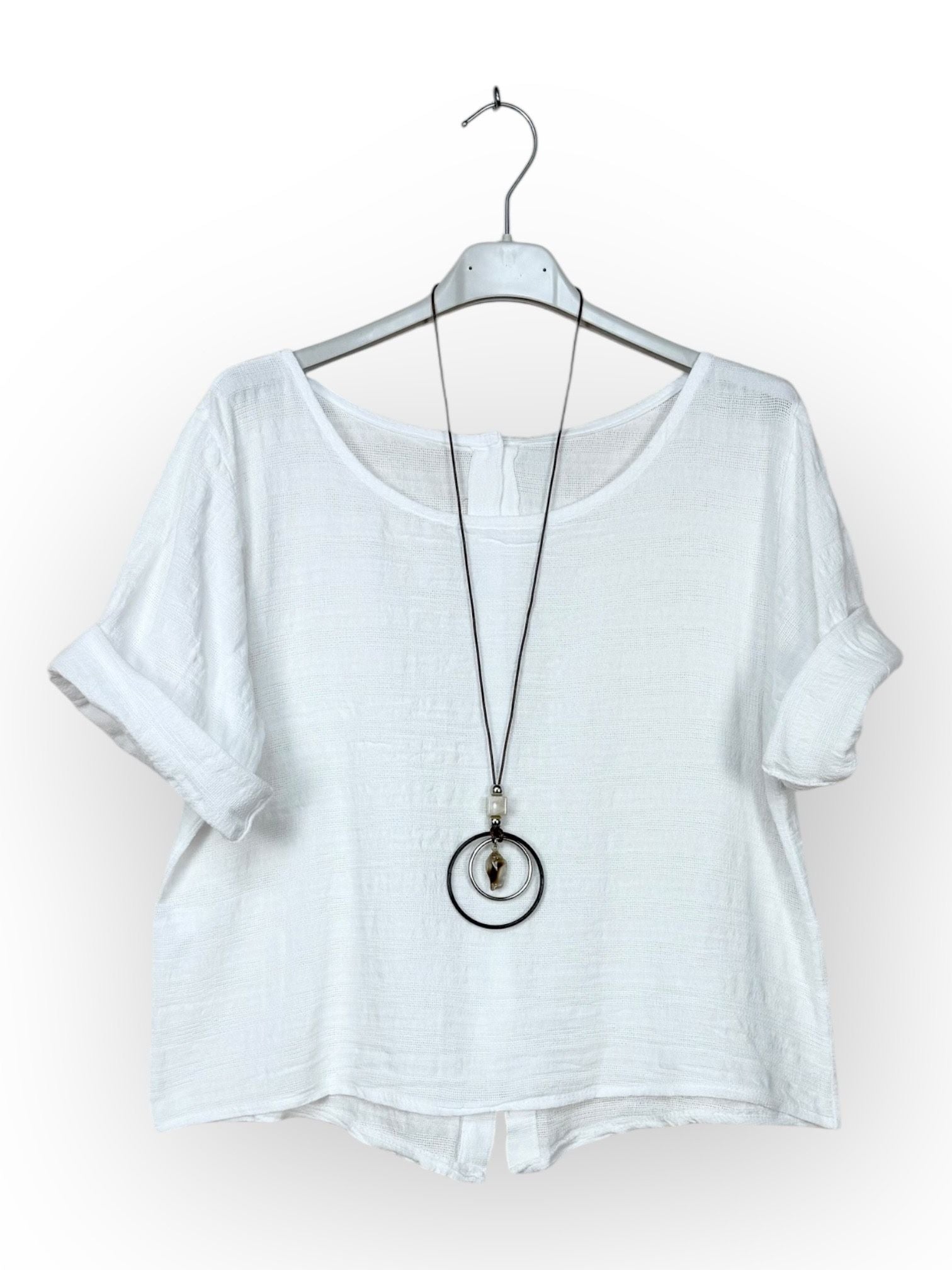 A white short-sleeve linen top hanging on a white hanger, styled with a long black pendant necklace featuring a silver-toned ring and a small gold-toned bead.