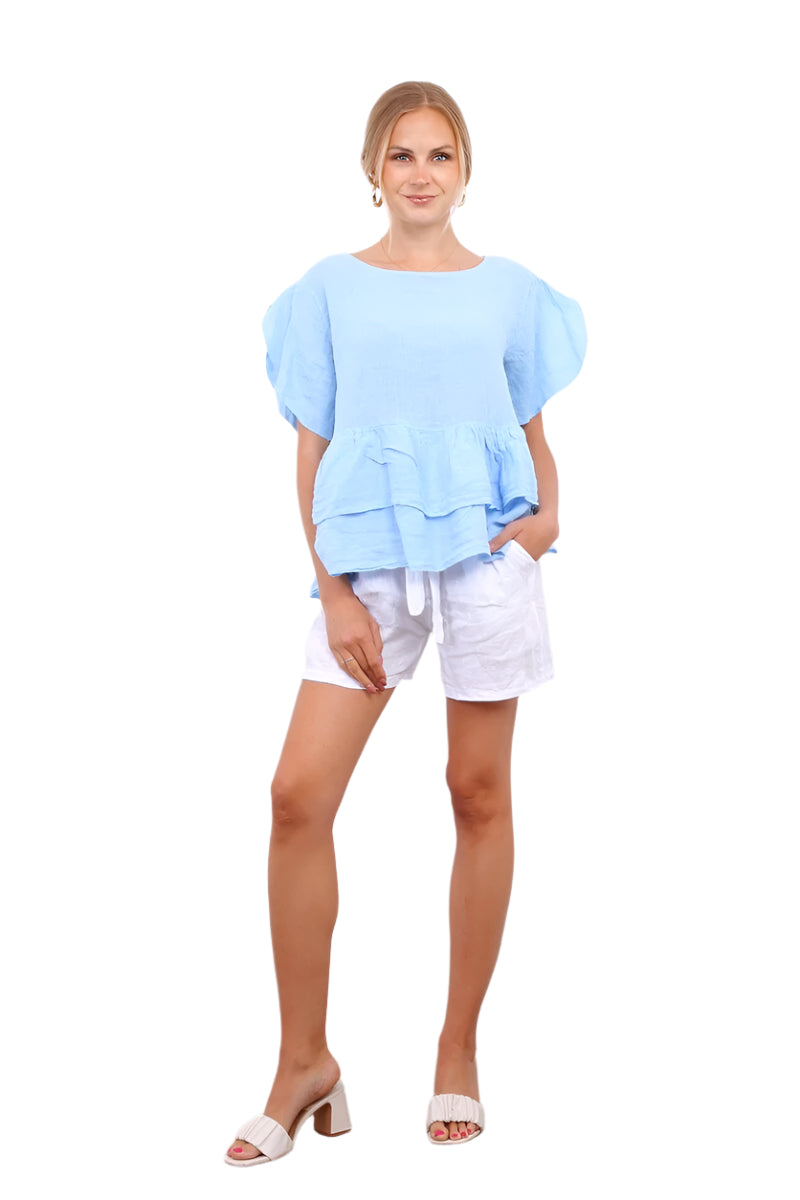 Woman wearing a light blue peplum top and white shorts standing against a white wall