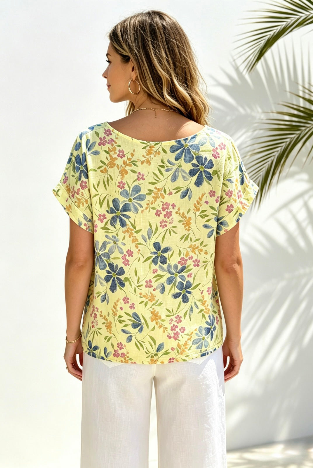 A woman shown from the back wearing a pale yellow short-sleeve top with a blue, green, and pink floral print, paired with white pants