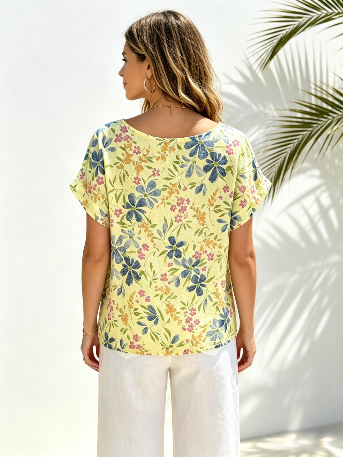 A woman shown from the back wearing a pale yellow short-sleeve top with a blue, green, and pink floral print, paired with white pants