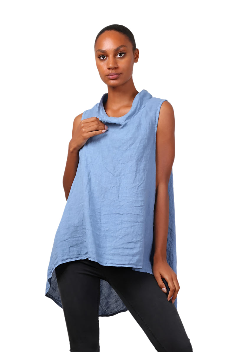 A woman wearing a denim blue sleeveless cowl neck top with an asymmetrical hem, paired with white trousers.