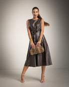 A woman models a sleeveless dark brown faux-leather midi dress with a tie waist, holding a snakeskin-patterned clutch bag, set against a neutral studio background.
