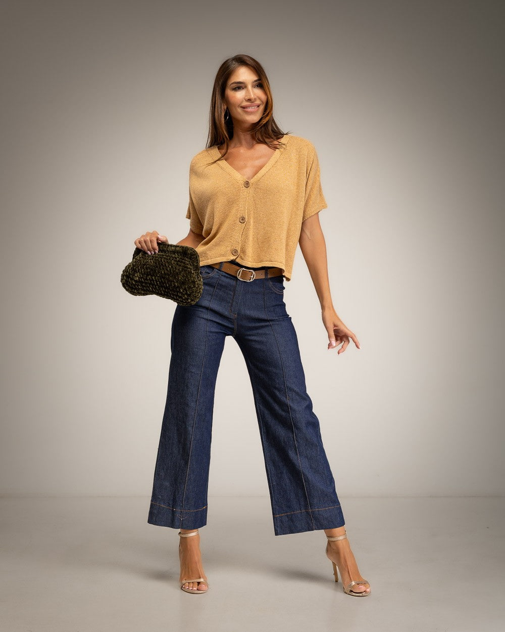 A woman modeling a camel short-sleeve button-up top and dark blue wide-leg jeans