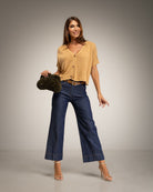 A woman modeling a camel short-sleeve button-up top and dark blue wide-leg jeans
