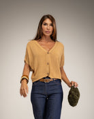 A woman modeling a camel short-sleeve knit cardigan with buttons, paired with dark blue jeans 
