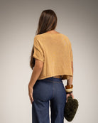 A woman shown from the back wearing a cropped, short-sleeve camel knit top and blue jeans
