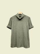 Green turtleneck top on a hanger against a plain background