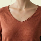 Close-up of a person wearing a rust-colored long-sleeve shirt with a neutral background