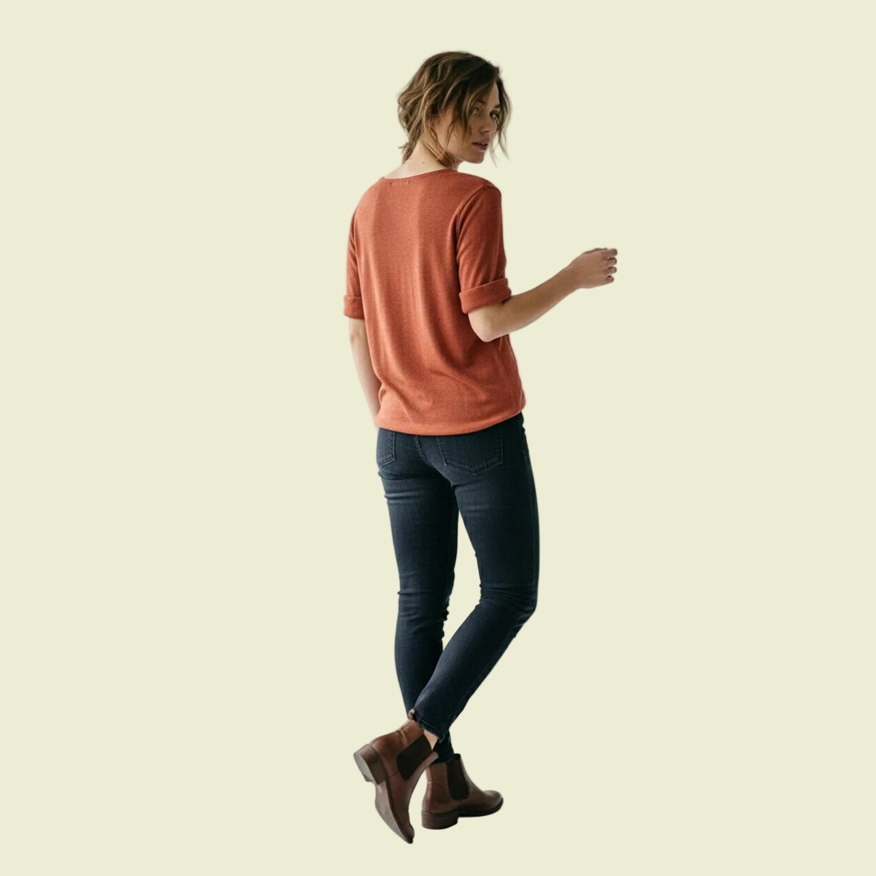 Woman wearing a rust-colored shirt and dark jeans on a white background