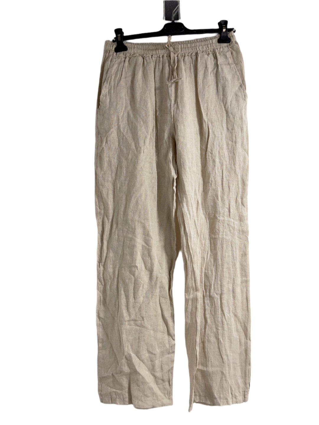 A woman standing against a white background wearing straight leg beige trousers with an elasticated waist, hung on a hanger with a white background