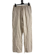 A woman standing against a white background wearing straight leg beige trousers with an elasticated waist, hung on a hanger with a white background