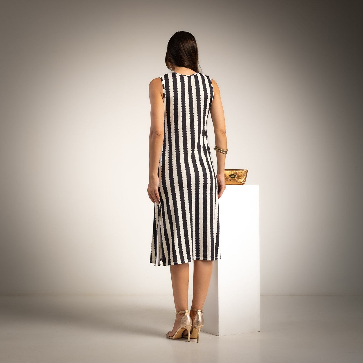 A woman stands with her back to the camera wearing a sleeveless black and white vertically striped midi dress