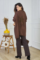 Woman wearing a brown cardigan with a star design in a room with a white wall and wooden floor.