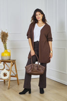 Woman in brown outfit holding a handbag in a room with white walls and wooden floor.