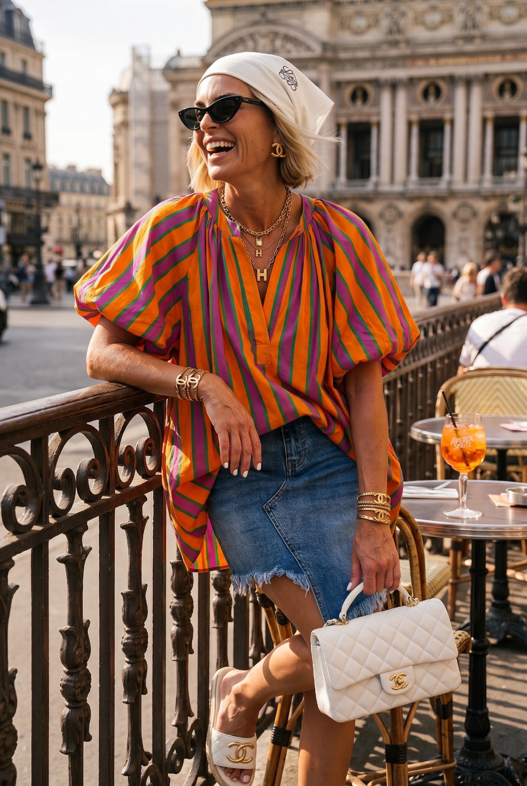 Woman in colorful striped shirt and denim skirt standing in an urban setting with a building in the background.