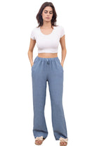 A woman standing against a white background wearing denim blue straight leg trousers with an elasticated waist, paired with a white top with a white background
