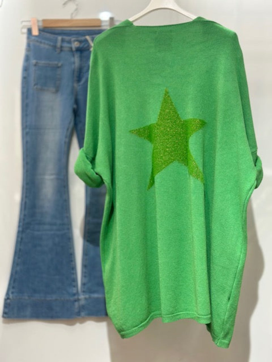 Green sweater with a star design and blue jeans on a white background