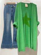 Green cardigan with a star design and blue jeans on a white background