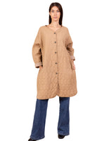 Woman wearing a beige quilted coat and blue jeans on a beige background