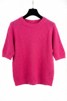 Pink sweater on a black hanger against a white background