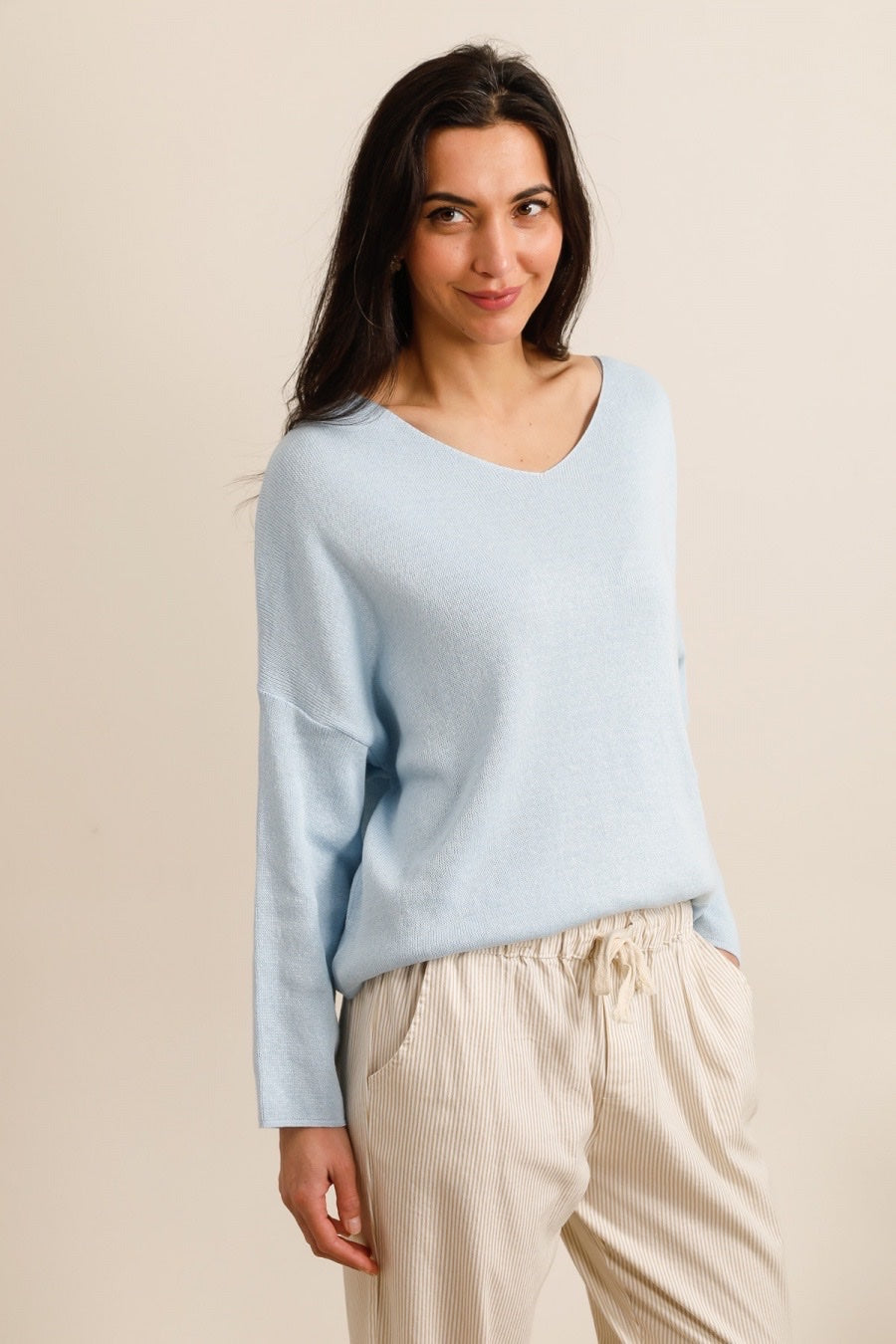Woman wearing a light blue sweater and beige pants against a beige background