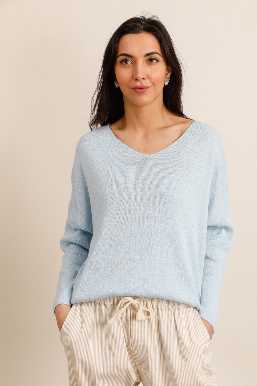 Woman wearing a light blue sweater and beige pants against a beige background
