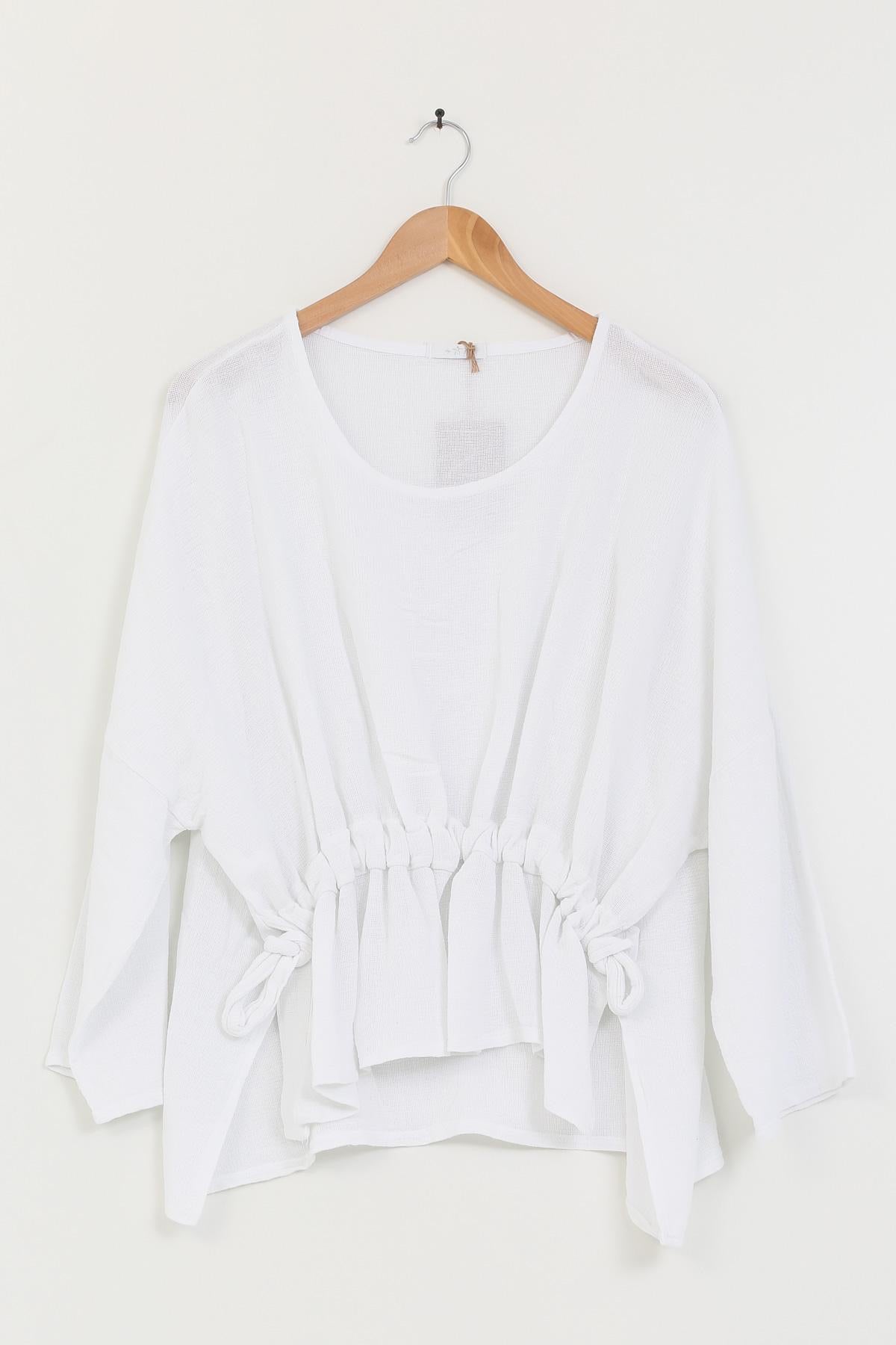 White linen tunic on a wooden hanger against a white background