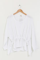 White linen tunic on a wooden hanger against a white background