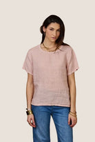 Woman wearing a light pink shirt and blue jeans against a beige background