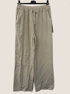 Beige cotton gauze pants on a hanger against a white wall