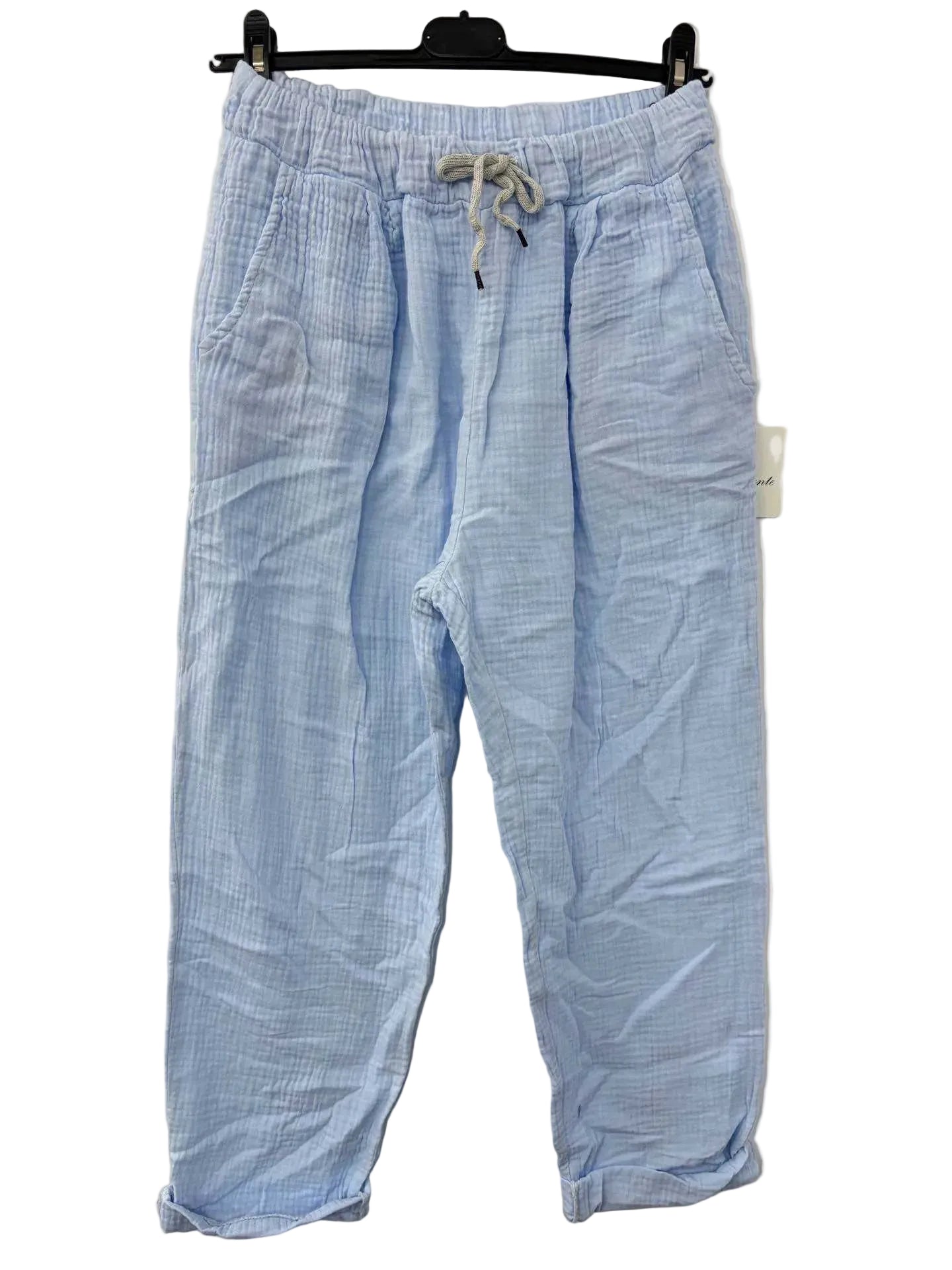 Sky Blue cotton gauze trousers on a hanger against a beige wall