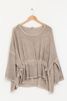 Beige linen tunic with tie details on a wooden hanger against a white background