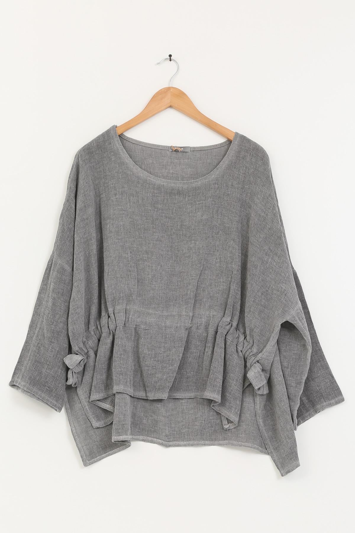 Gray linen tunic with ruffled details on a wooden hanger against a white background