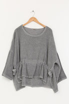 Gray linen tunic with ruffled details on a wooden hanger against a white background