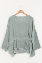 Duck green linen top on a wooden hanger against a white background