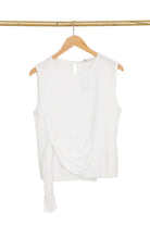 White sleeveless top on a wooden hanger against a white background