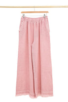 Rose wide-leg pants hanging on a wooden hanger against a white background
