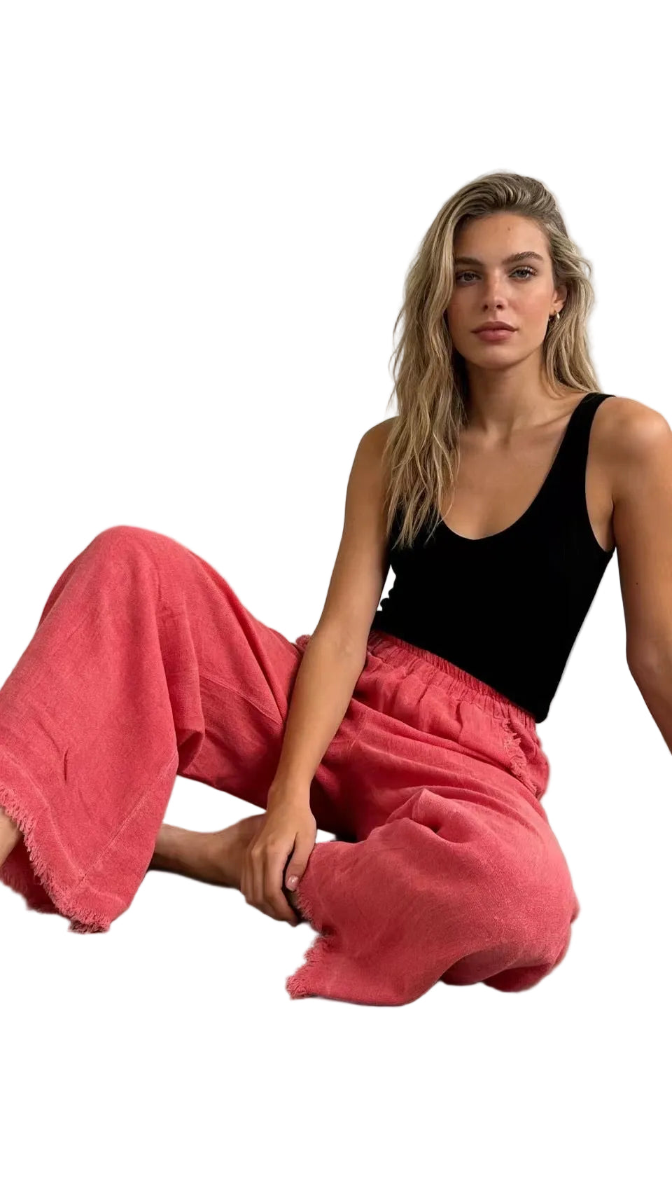 Woman wearing a black tank top and coral pants sitting on the floor against a white background