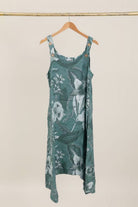 Green floral dress hanging on a wooden hanger against a beige background