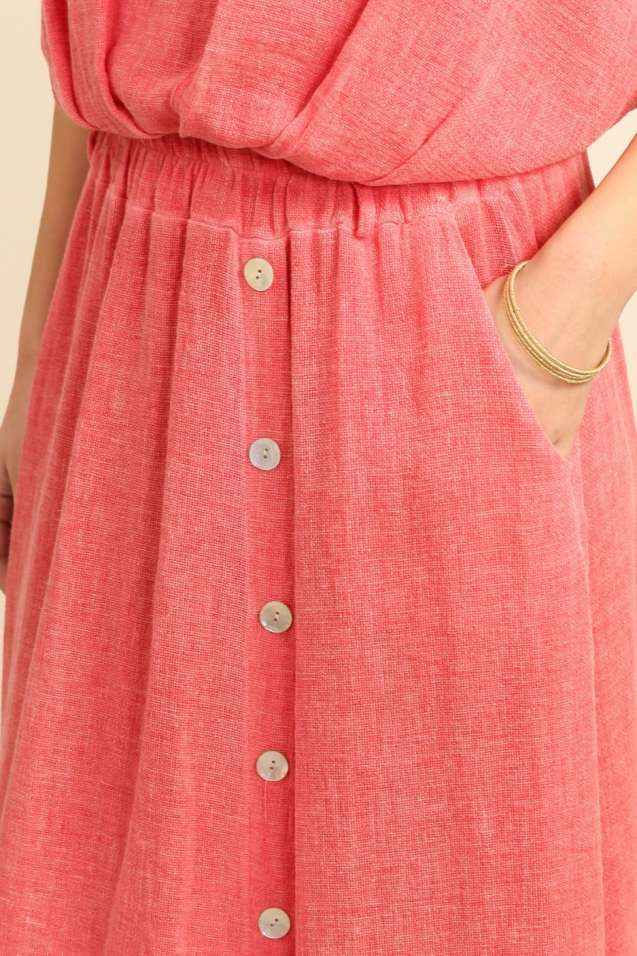 Close-up of a coral pink top & skirt with buttons on a beige background 