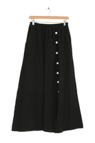 Black skirt with white buttons on a hanger against a white background