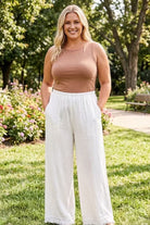 Woman wearing a brown top and white pants standing in a park.