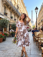 Woman in a floral dress standing on a Paris street with the Eiffel Tower in the background.