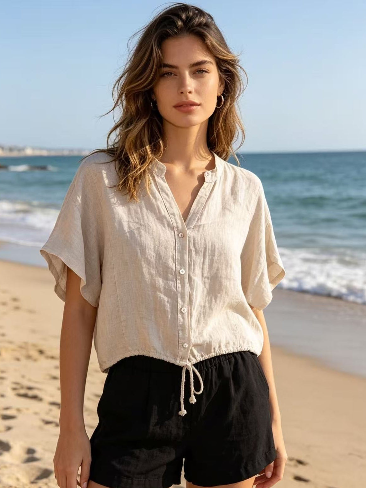 Woman wearing a light-colored shirt and black shorts on a beach with ocean in the background