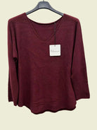 A women's long-sleeve knit sweater in a deep burgundy or maroon color, hanging on a black hanger against a plain white background. 