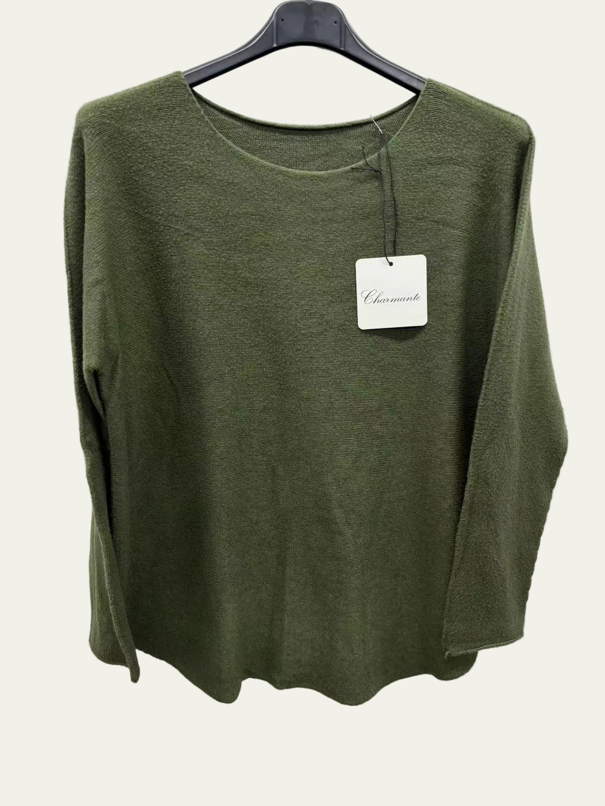 A green long-sleeve knit top hanging on a black hanger against a plain white wall, 