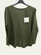 A green long-sleeve knit top hanging on a black hanger against a plain white wall, 