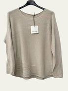 A light beige knit long-sleeve top hanging on a black hanger against a white wall,